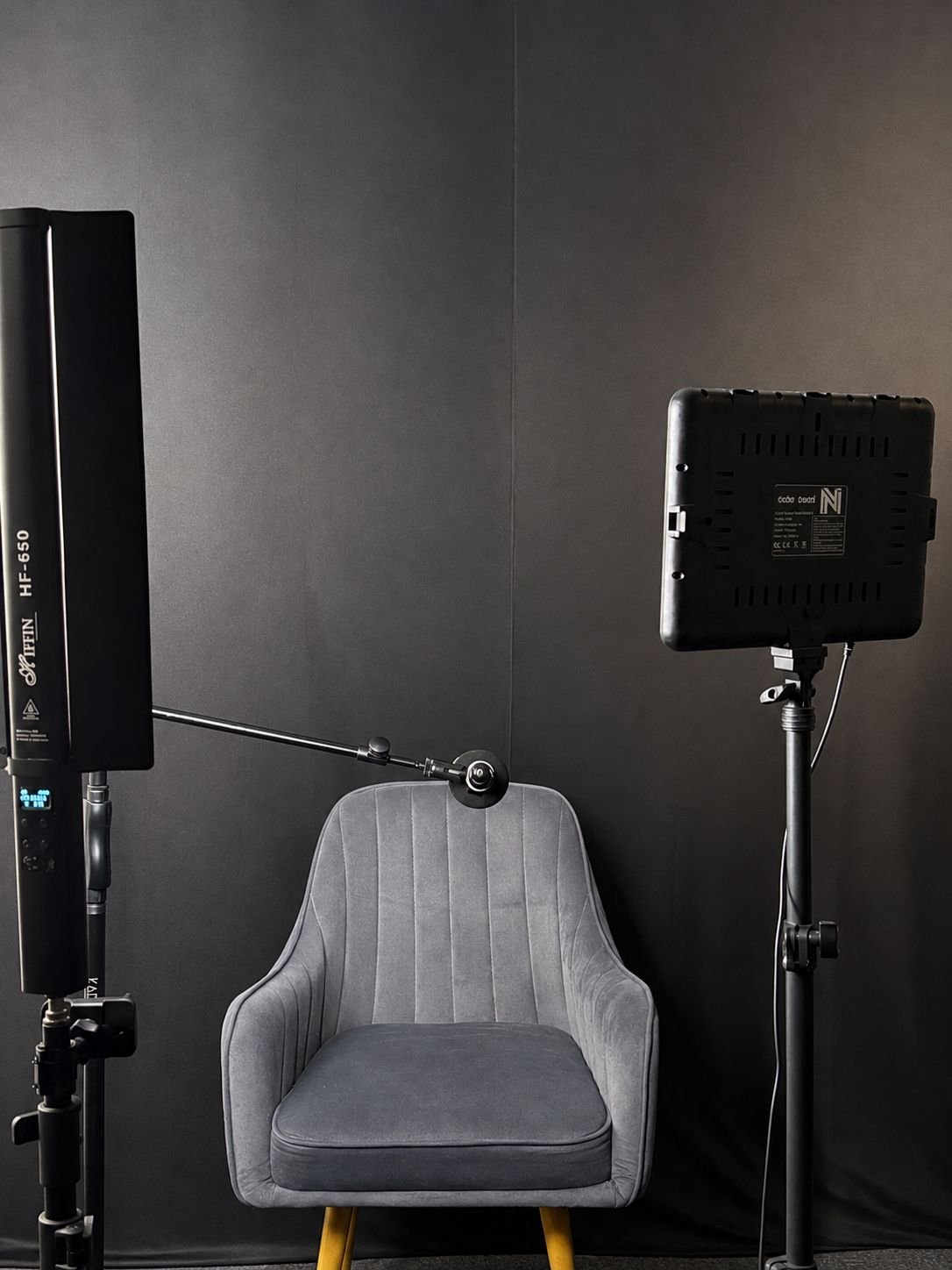 The podcast studio at The Fourth Room: a grey armchair against a dark backdrop, with an LED panel light on a stand, a tall tube light and a boom arm.